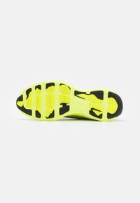 Semelle de chaussure de sport jaune vif et noire avec motifs texturés antidérapants, vue du dessous sur fond blanc.
