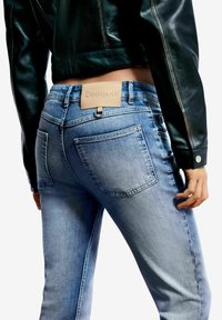 Vaqueros de mezclilla azul claro con un corte ajustado, que cuentan con bolsillos traseros y una etiqueta de cuero marrón en la cintura. Textura suave y diseño clásico.