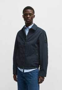 Giacca leggera di colore blu navy con zip frontale, colletto e tasche laterali. Materiale in misto cotone con una texture morbida.