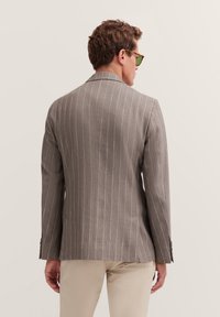Graue gestreifte Jacke mit taillierter Passform, die hellfarbige Streifen und einen Schlitz auf der Rückseite aufweist, kombiniert mit beigen Hosen.
