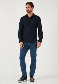 Cămașă albastră cu butoni, cu mâneci lungi, asortată cu blugi denim albaștri și adidași cu accente gri. Culoare solidă cu o textură netedă.
