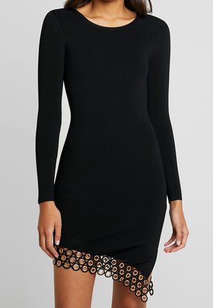 Zwarte jurk met lange mouwen, ribbelige textuur en een geschulpte zoom met ronde uitsparingen en gouden accenten langs de onderrand.