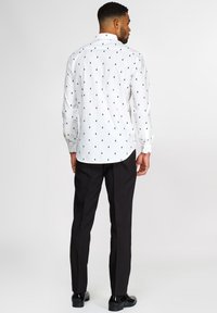 Camicia bianca a maniche lunghe con un motivo di alberi verdi, colletto e polsini bottonati, abbinata a pantaloni e scarpe neri.