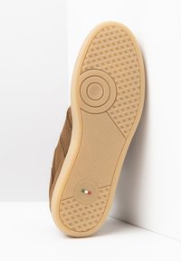 Scarpa in suede marrone con suola in gomma, caratterizzata da un motivo testurizzato e un accento circolare. Logo impresso vicino al tallone con la bandiera italiana.