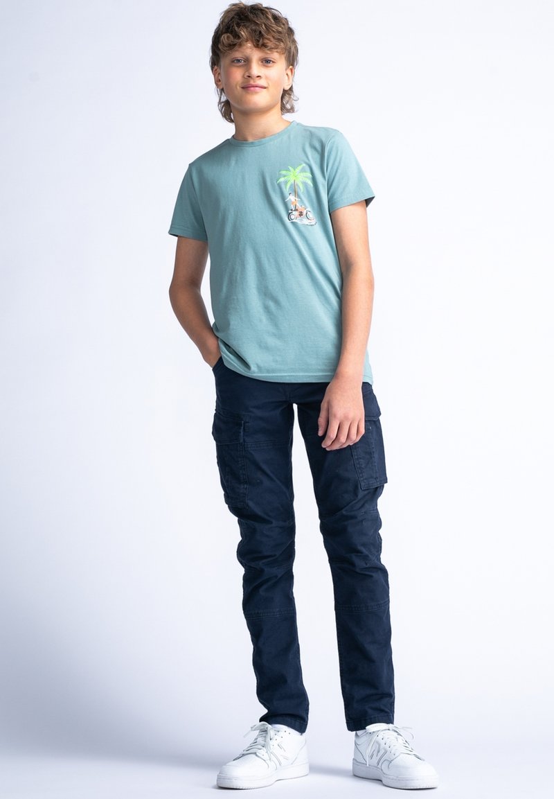 Svetle modré bavlněné tričko s grafikou palmy, kombinované s námořnickými kapsáčovými kalhotami a bílými teniskami, které mají několik kapes a volný střih.