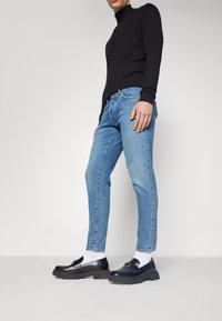 Top negro de manga larga, vaqueros azul claro y mocasines negros con suela gruesa, combinados con calcetines blancos. Ajuste simple y moderno.