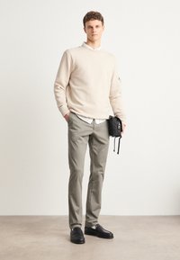 Beige sweatshirt, grå bukser og sorte loafers. Hvid skjorte under, med en lille sort taske i hånden. Enkel og moderne design.