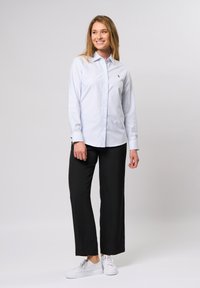 Heledat sinine triibuline nööbiga särk väikse logoga, kombineeritud mustade laiade pükstega ja valgete tossudega. Sile puuvillane kangas.