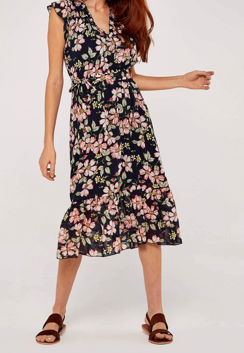 Robe midi florale avec un fond marine, ornée de fleurs roses et vertes, des manches volantes, une taille cintrée et un ourlet inférieur à volants. Sandales marron.