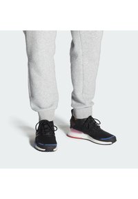 Black athletic shoes with blue and red accents, textured mesh upper, laces, and a cushioned sole. Worn with gray sweatpants.