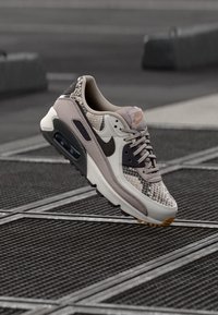 Nike Air Max 90, con tomaia in mesh beige e grigio, dettagli neri e stampa effetto pelle di serpente testurizzata. Ammortizzazione Air visibile nella suola.