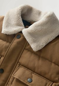 Pruun polsterdatud jakk, millel on beež sünteetiline karusnahkrajatisega krae, kaks esipaneeli taskut nupuga kinnitustega ja tekstuuriga kangast viimistlus.