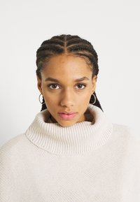 Maglione lavorato a maglia color beige chiaro con colletto alto a coste, caratterizzato da un motivo testurizzato e una vestibilità ampia e rilassata.