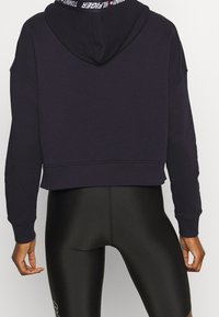 Sudadera corta azul marino con una banda elástica con logo, material de mezcla de algodón, mangas largas y capucha con cordón. Usada con leggings negros.