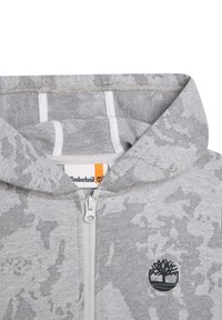 Šedá maskáčová zipová mikina s hladkou texturou, s černým logem, bílým zipem a kontrastní podšívkou.