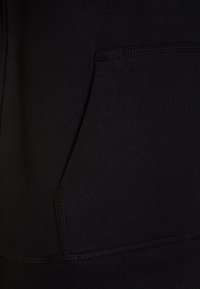 Czarna bluza z kapturem z przednią kieszenią. Charakteryzuje się miękką teksturą, przeszytymi szwami oraz prostym wzornictwem bez logo i wzorów.