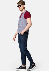 Szary kamizelka w kratę noszona na burgundowej koszulce, w połączeniu z podartych ciemnych dżinsach i czarnych trampkach. Na dodatki składają się ciemne okulary przeciwsłoneczne.