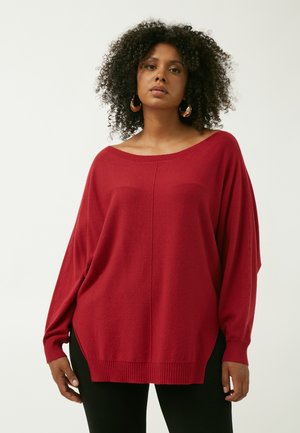 Rød oversize sweater lavet af blødt stof, med en bred halsudskæring, forlængede ærmer og ribbede kanter og manchetter. Ingen mønstre eller accenter.