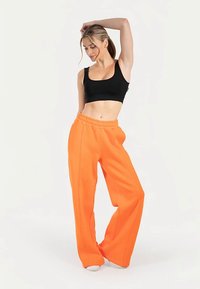 Sort croptop og orange vidde bukser i sweatshirt-stof. Bukserne har snøre i taljen og en glat overflade med synlige sidesømme.