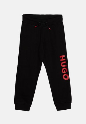 Pantalones de chándal negros con cordón, puños elásticos y "HUGO" impreso verticalmente en rojo en la pierna izquierda.