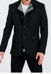 Czarna marynarka z szarym kołnierzem, dwoma kieszeniami na suwak i jedną kieszenią na piersi. Wykonana z teksturowanej tkaniny. Zapięcie na guziki z przodu.