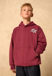 Felpa con cappuccio color granata con tasca frontale e ricamo bianco "LA" sul petto. Presenta una tasca a marsupio e polsini a costine. Tessuto dalla texture morbida.