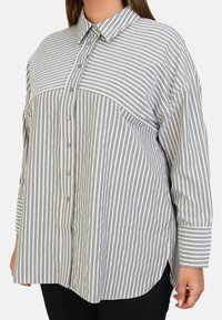Chemise à rayures gris et blanc, dotée d'un col, de manches longues et d'une coupe décontractée. Tissu doux avec une texture agréable.