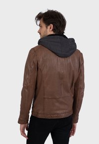 Giacca di pelle marrone con cappuccio grigio, caratterizzata da una superficie testurizzata, cuciture dettagliate e una vestibilità aderente. Design minimalista nel complesso.