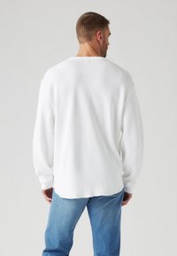 Hvit stripete langermet skjorte med en avslappet passform, med senkede skuldre og en buet nederkant, paret med lyseblå denimjeans.