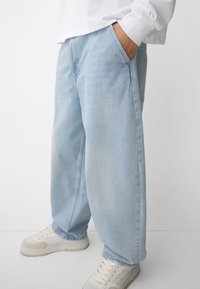 Svietlo modré voľné jeansy z denimu, s bočnými vreckami a uvoľneným strihom, kombinované s bielymi teniskami.