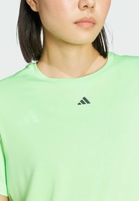 Zelené sportovní tričko vyrobené z hladké tkaniny. Kulatý výstřih s krátkými rukávy. Na oblasti hrudníku se nachází tmavě šedé logo.