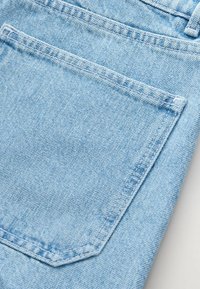 Vaalea sininen denim-kangas, jossa on takatasku näkyvällä ompeleella, pehmeä rakenne ja hieman haalistunut ulkonäkö.