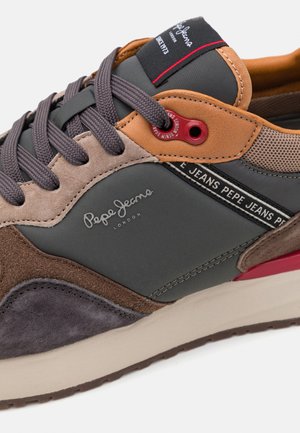 Sneaker featuring a mix of gray, brown, and tan materials, with textured suede and smooth fabric. Accented with red hardware and logo detail.