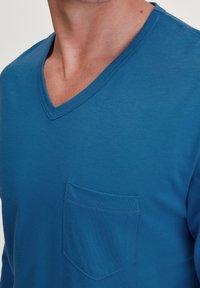 T-shirt en coton bleu à manches courtes et décolleté en V, avec une poche plaquée sur la poitrine gauche, texture douce et coupe classique.