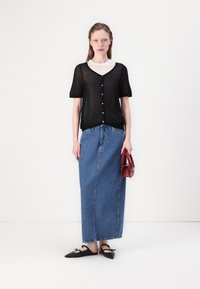 Svart kortärmad, genomskinlig stickad topp med knappar framtill; matchad med en lång blå denimkjol och svarta ballerinas. Röd handväska ger kontrast.