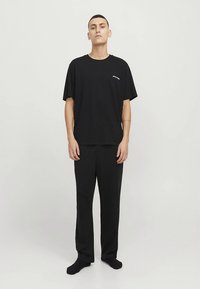 Sort bomuld t-shirt med afslappet pasform og lille hvidt logo, kombineret med sorte bukser. Glat tekstur, minimalistisk design, uden mønstre.