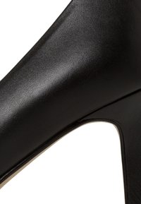 Svart lær høye hæler med en glatt tekstur, spiss tå og utskåret design på siden for en elegant silhuett.