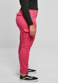 Rosa cargobyxor med smal passform, elastiska muddar och sidofickor, ihopparade med svarta sneakers. Tyget verkar slätt med en viss lyster.