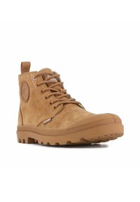 Botas de ante marrón claro hasta el tobillo con puntera redonda, parte frontal con cordones y suela de goma con un dibujo texturizado. Incluye un logo en el lateral y una tira para facilitar el calzado.