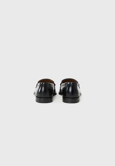 Black leather loafers with smooth texture, back view showing rounded edges and a low stacked heel. Minimalistic design with no visible adornments.