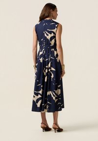 Sleeveless navy dress with cream abstract pattern, cinched waist, flowing skirt, and ankle-length hem. Worn with animal print heels.