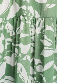Tejido verde y blanco con un patrón floral; presenta pliegues y un acabado ligero y texturizado.