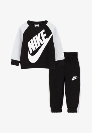 Must ja hall Nike dressipluus suure logoga, sellega sobitatud mustad dressipüksid, millel on logo reie piirkonnas. Elastsed mansetid ja vöökoht.