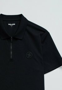 Polo negro de manga corta con cremallera frontal y logo redondo en relieve en el pecho izquierdo, etiquetado como "Salsa Jeans Slim Fit" talla grande.