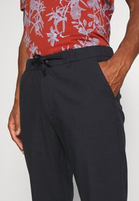 Navy relaxed-fit pants made of lightweight fabric, featuring an elastic waistband with a drawstring and side pockets.