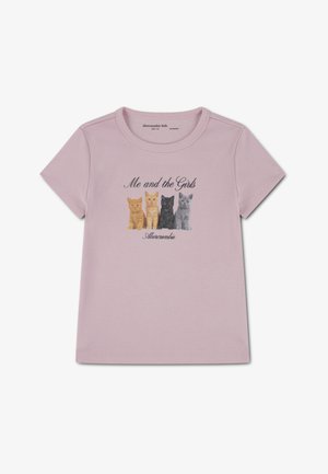 Světle růžové tričko z měkké látky s potiskem na přední straně zobrazujícím čtyři ilustrované kočky v oranžové, černé a šedé barvě. Nad potiskem je nápis "Já a holky."