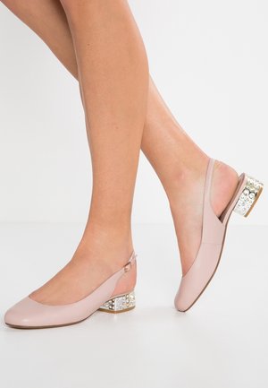 Kobieta nosząca jasnoróżowe buty typu slingback na niskim słupku ozdobione przezroczystymi i perłopodobnymi kamieniami.