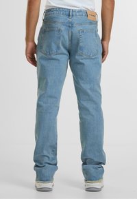 Šviesiai mėlynos džinsinės kelnės su tiesiu kirpimu, turinčios dvi užpakalines kišenes ir odinį etiketę juosmens srityje. Paskutiniai kraštai įrėžti.