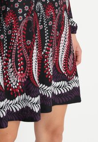 Vestido de manga larga en tela negra con patrones de paisley y flores en rojo, blanco y púrpura, con un dobladillo a mitad del muslo.
