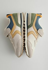 Sneakers har en blanding af cremefarvet syntetisk materiale med grønne, blå og orange detaljer, tekstureret ruskind og en kontrasterende gummisål.